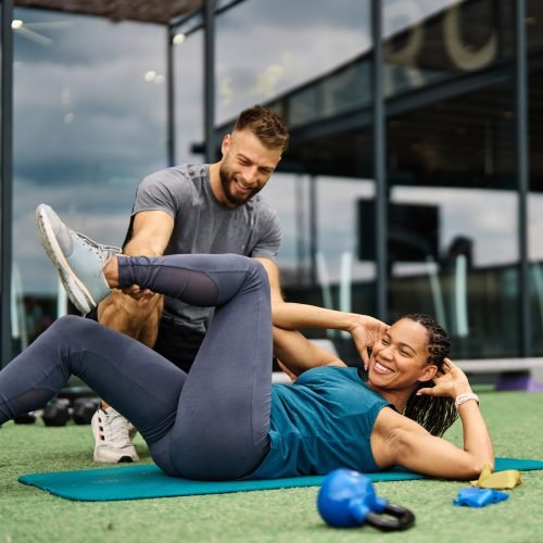 Portrait of  healthy fit woman duing crunches at the gym supprted by a trainer instructor exercising in fitness club