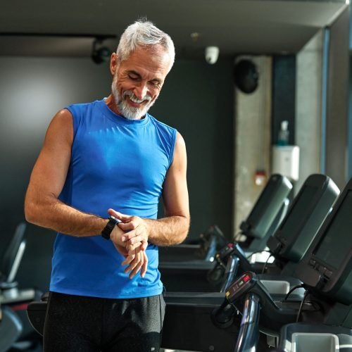 Portrait of a senior man exercising in a gym, mature male running using treadmill machine and checking smart watch for performance, healthy lifestyle and cardio exercise at fitness club concepts, vitality and active senior