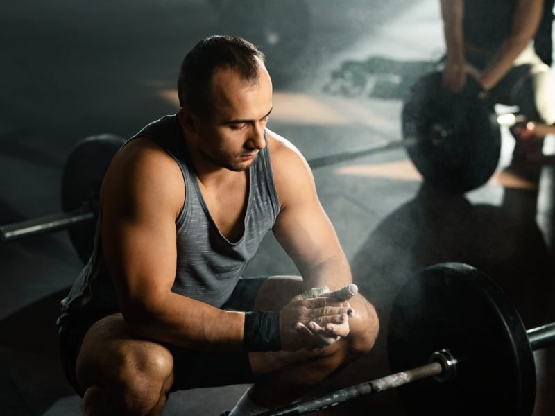 Young bodybuilder preparing for a deadlift and clapping his hands with sports chalk in a gym.