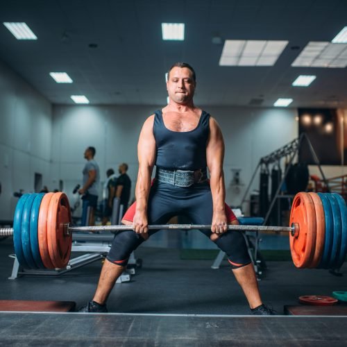Strong weightlifter doing exercise with barbell, deadlift, gym interior on background. Weightlifting workout in sport or fitness club, bodybuilding