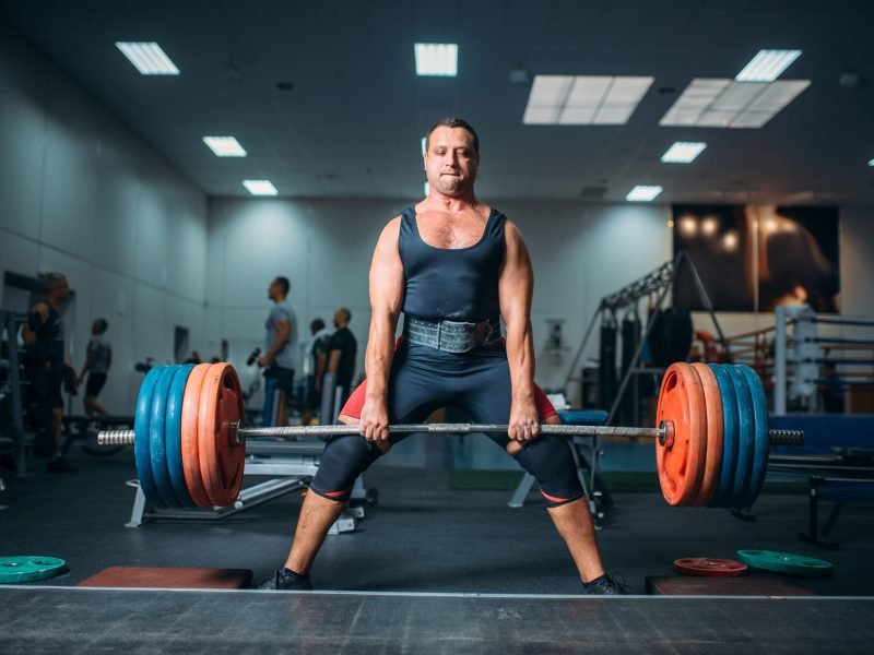 Strong weightlifter doing exercise with barbell, deadlift, gym interior on background. Weightlifting workout in sport or fitness club, bodybuilding